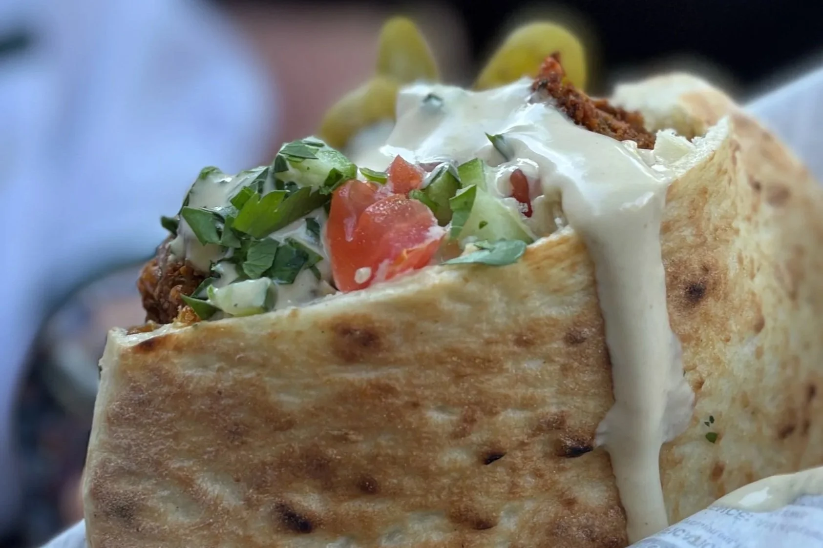 Close-up of a taco with cream, chopped vegetables, shredded meat, and a crispy tortilla shell.