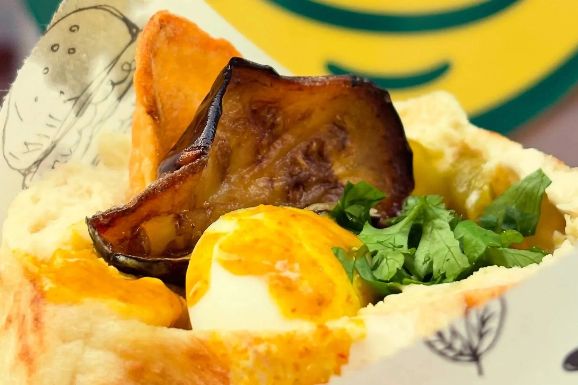 Close-up of a plate with breakfast foods including fried eggs, roasted potatoes, hash browns, and green salad, on a patterned dish with a yellow and green background.