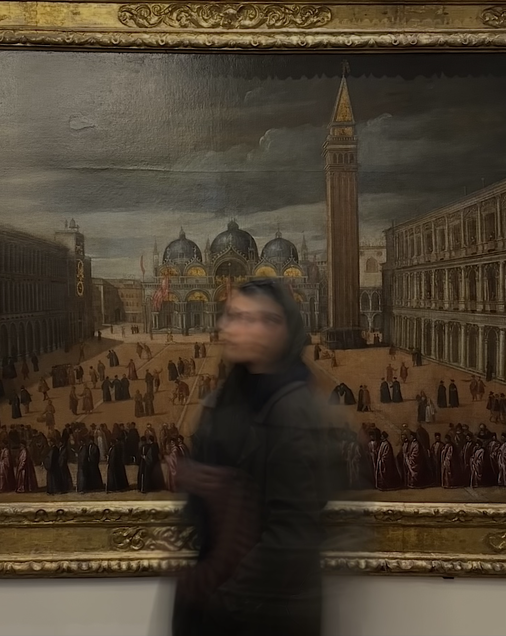 A person standing in front of a large painting of Venice, Italy, featuring St. Mark's Square, the Basilica di San Marco, and the Campanile. The person is blurred, indicating motion, and is wearing dark clothing with a head covering.