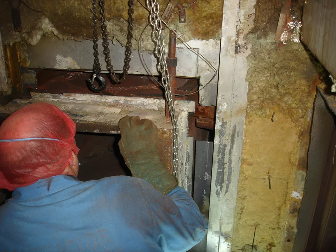 Engineer working at an opened industrial oven assembly, with exposed insulation and lifting chains visible.