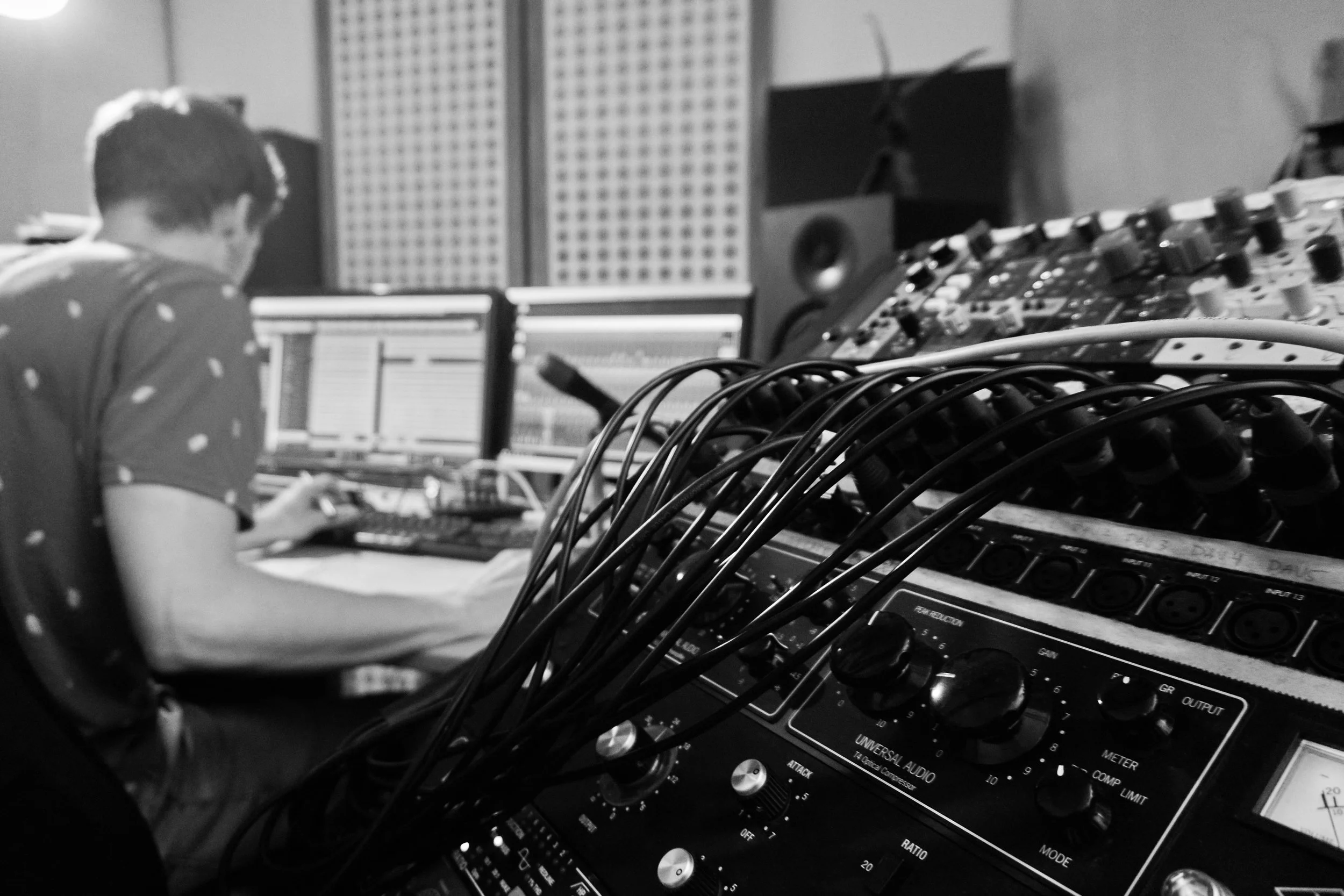 Ein Musikproduzent arbeitet an einem Musikmischpult in einem Tonstudio, mit mehreren Monitoren und Audiogeräten.