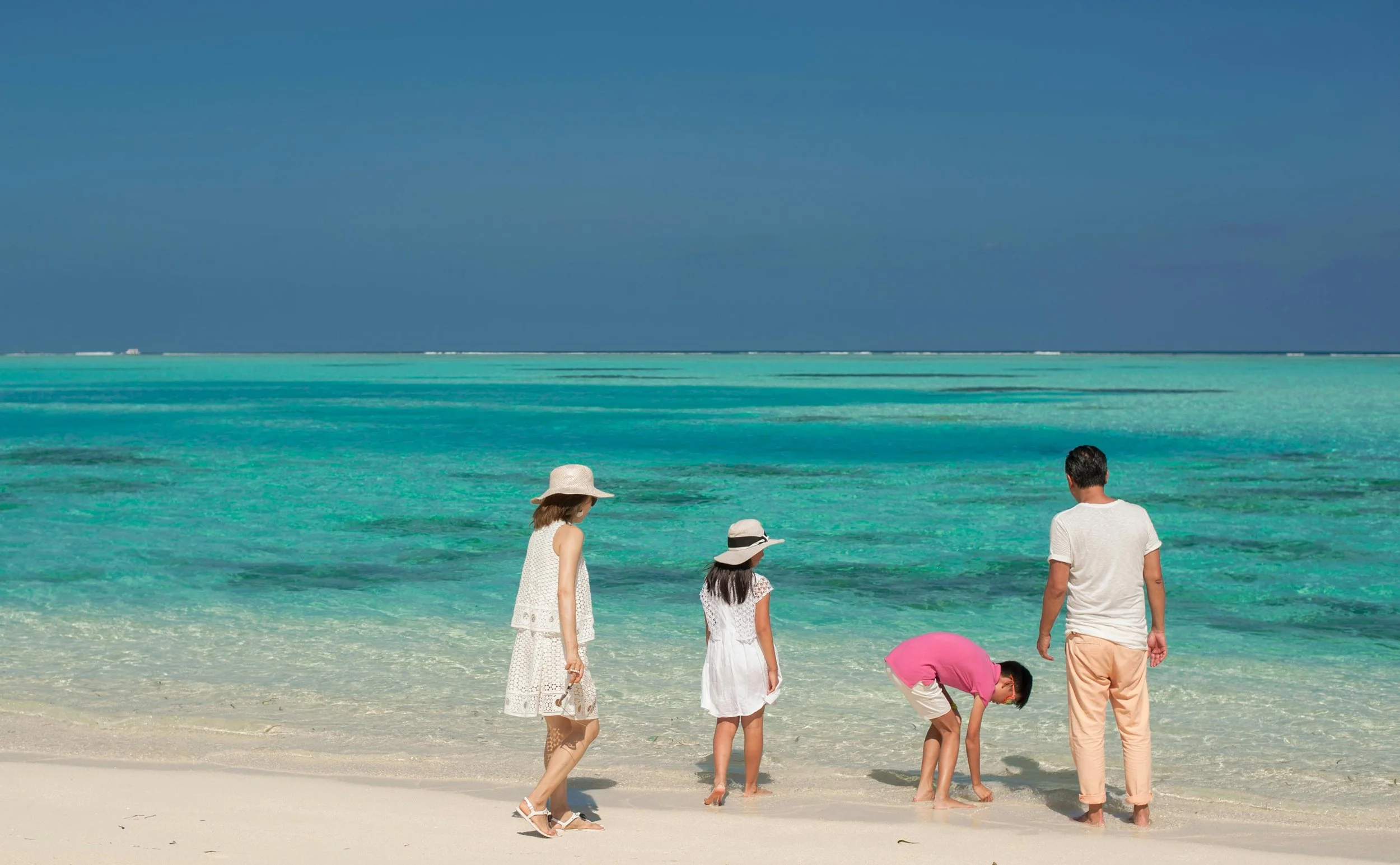 Family enjoying a day at the beach in the Mediterranean, with turquoise water, white sand, and a clear blue sky.