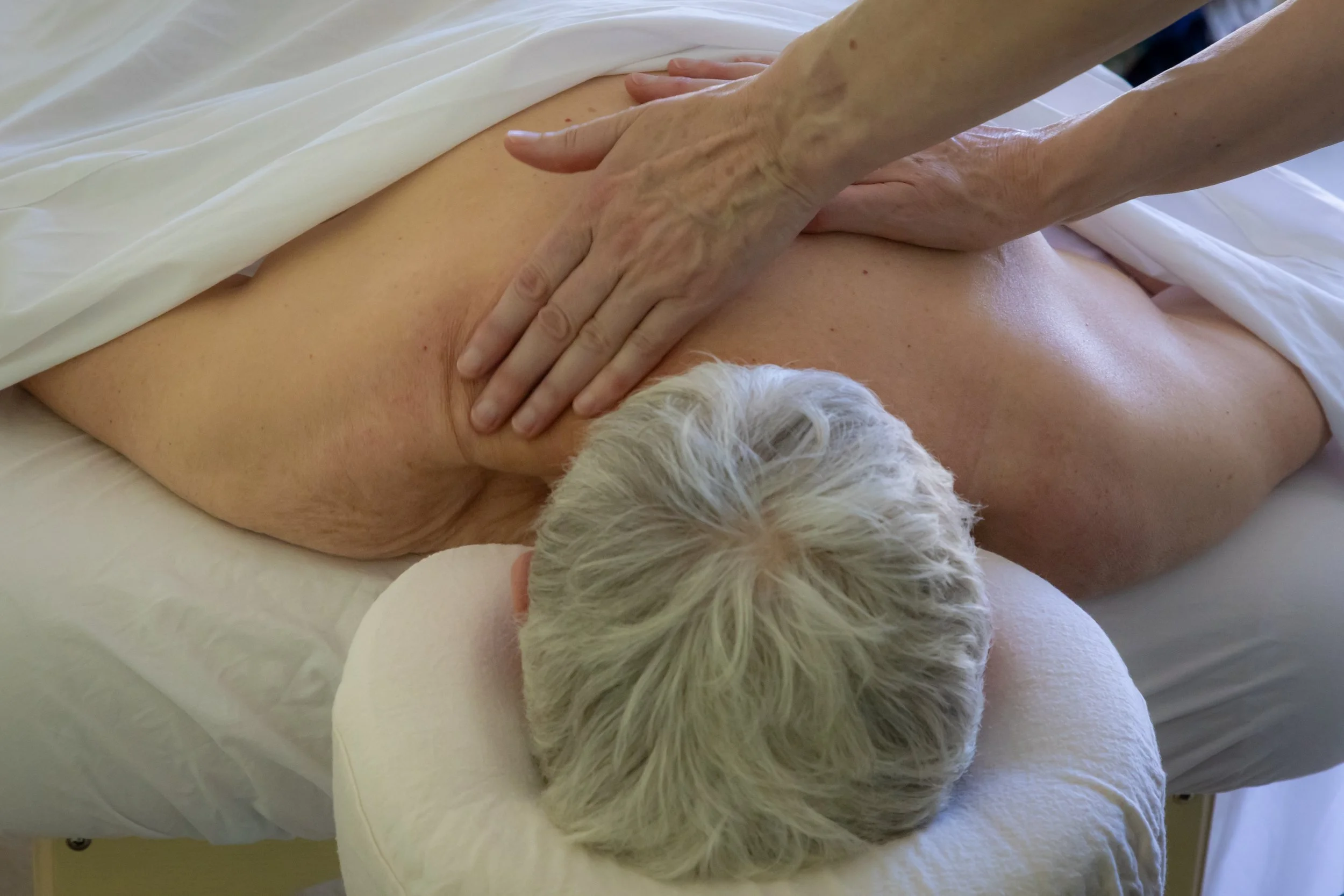 A woman face down on a massage table receiving a relaxing massage to her shoulders