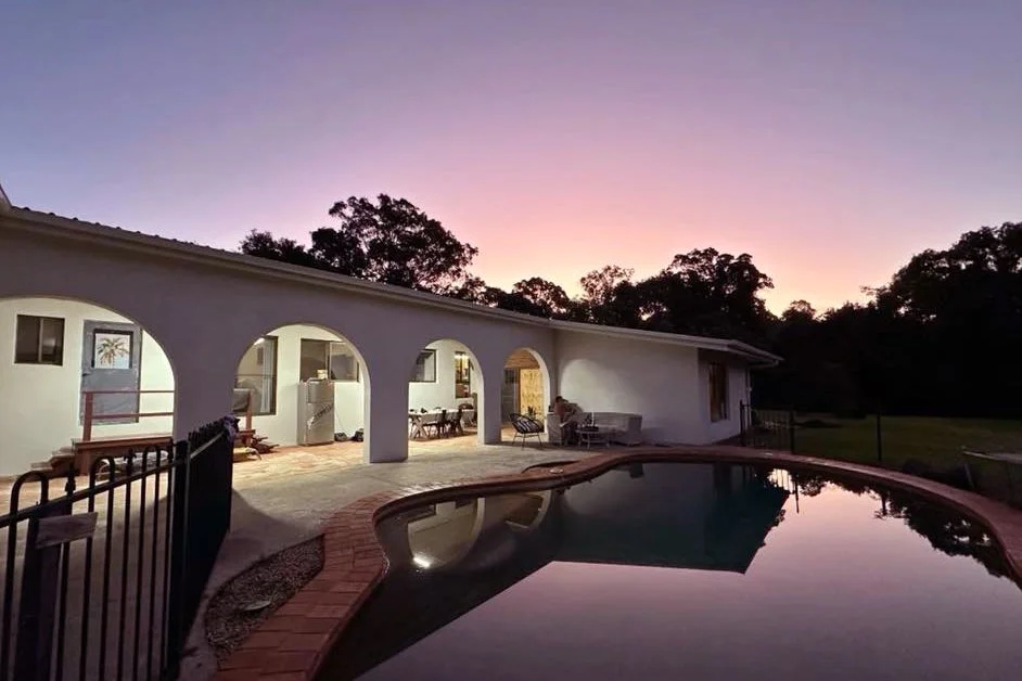 A house with archways, outdoor furniture, and a swimming pool at sunset.