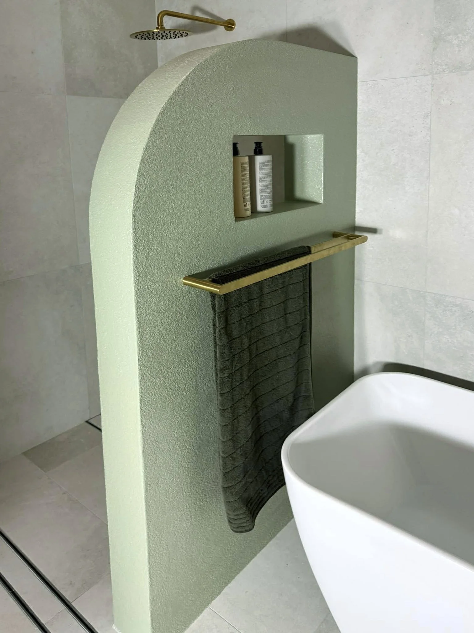 A bathroom scene with a showerhead, a towel hanging on a gold-colored bar, and a white free-standing bathtub.
