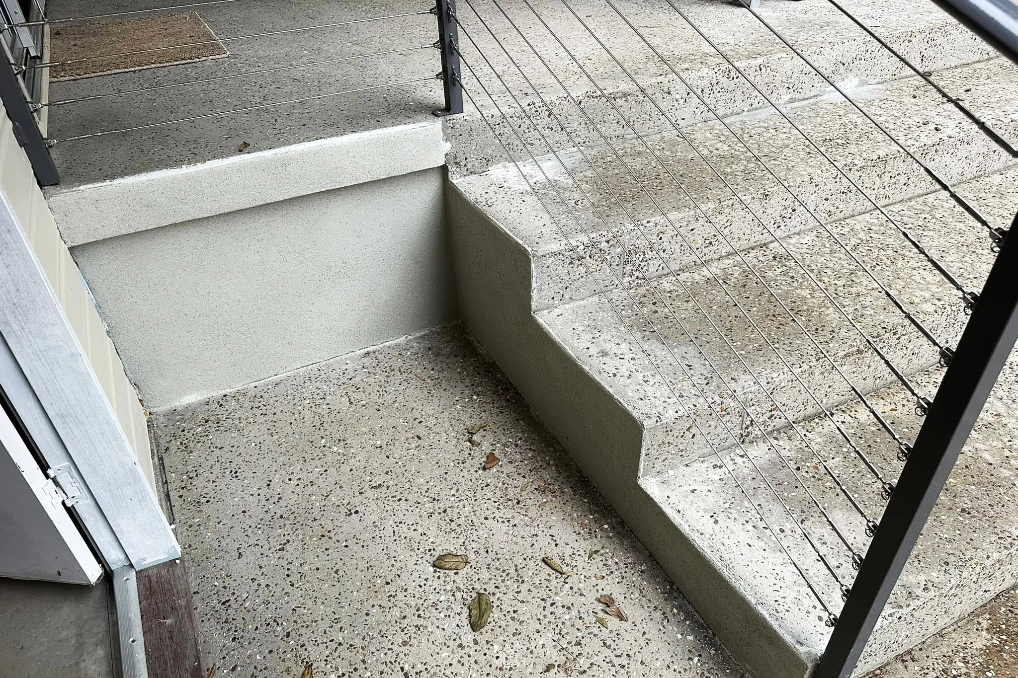 Concrete stairs with metal railing and scattered fallen leaves outside a building, with a concrete porch and steps leading up.