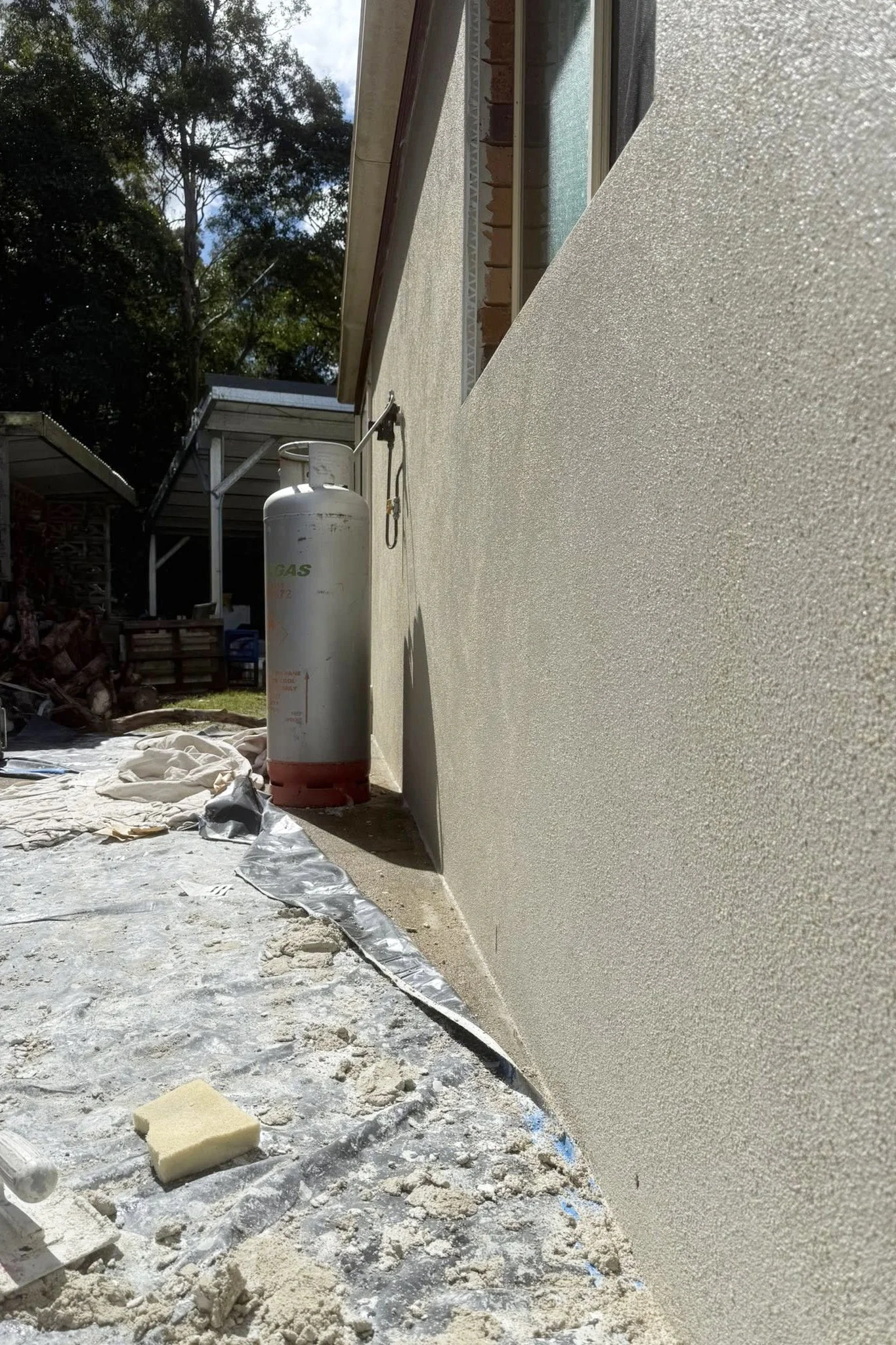 Exterior wall under construction with a propane tank, construction debris, and insulation on the ground.