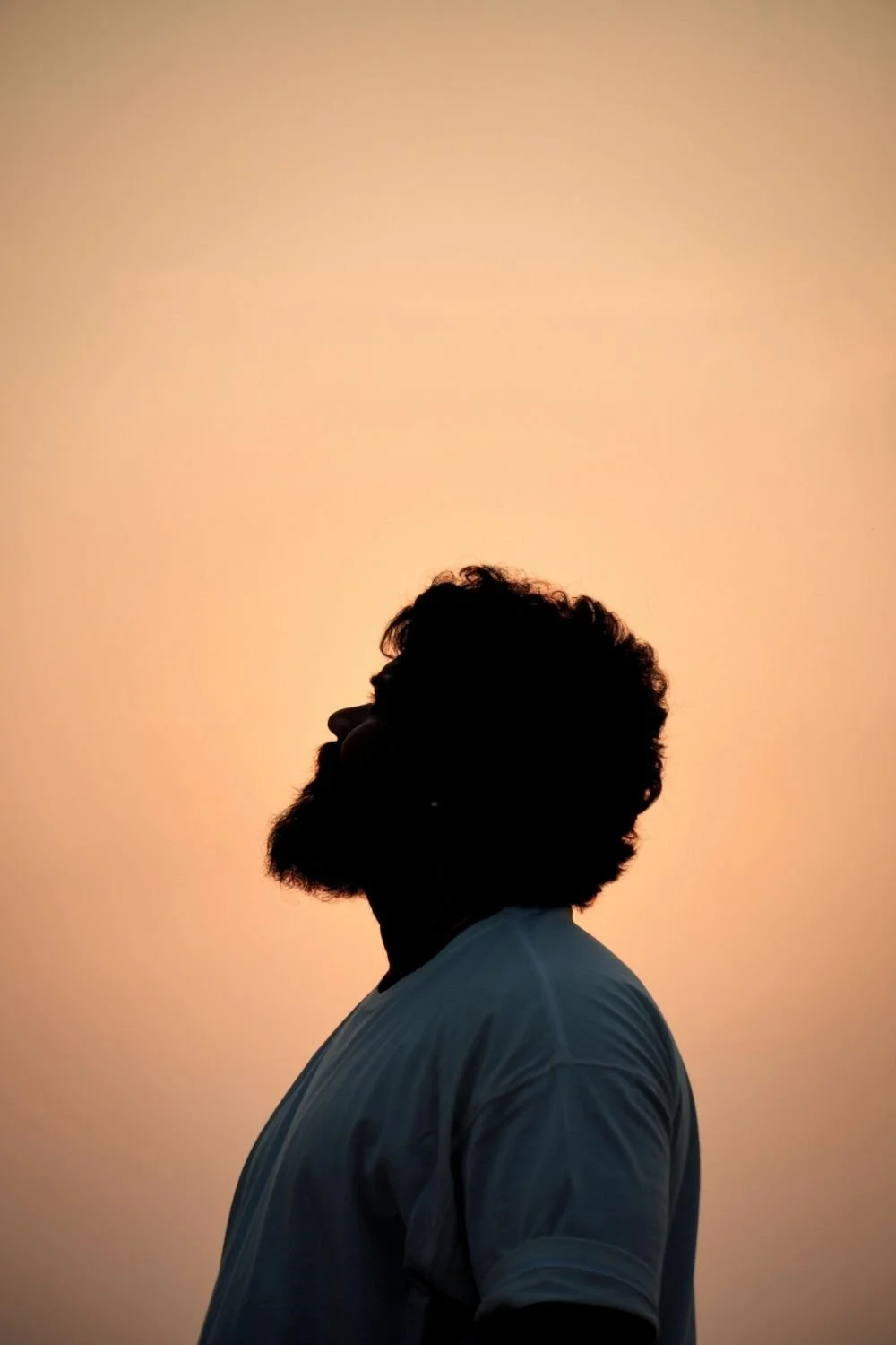 Silhouette of a bearded person looking upward against a warm sunset sky, symbolizing confidence, purpose, self confidence training, and personal growth coaching.