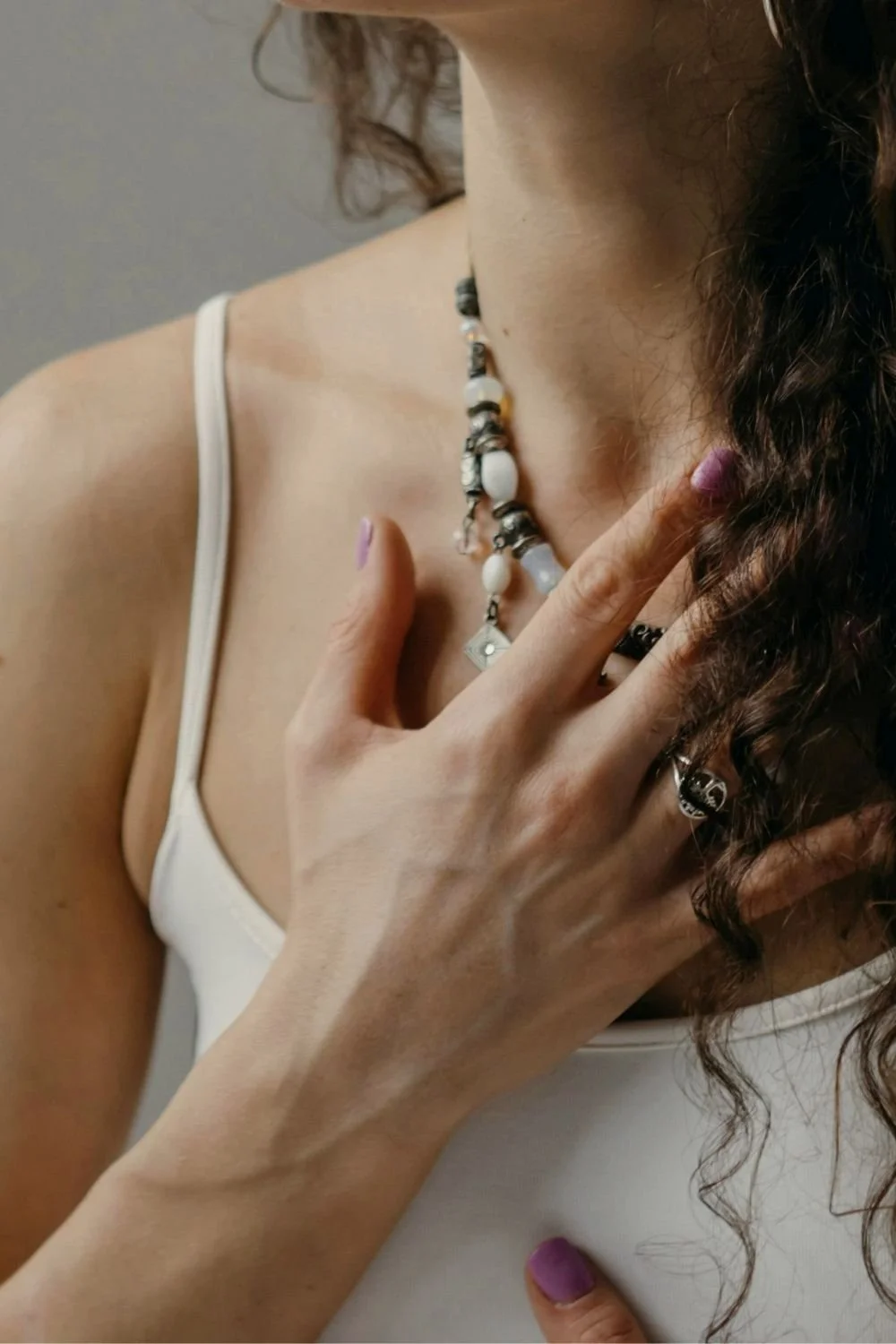 Close-up of a person gently resting a hand on their chest while wearing a beaded necklace, conveying self-awareness, compassion, emotional support coaching, and inner healing training.