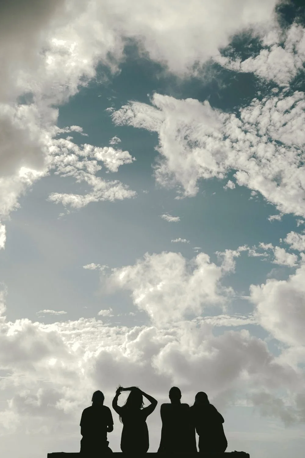 Silhouettes of several people gathered beneath a vast sky filled with clouds, representing community, connection, learning, and shared experiences in personal development seminars focused on growth and self-confidence.