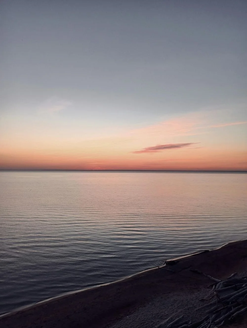 Peaceful sunset over calm water with soft pink and orange hues reflecting across the horizon, creating a serene atmosphere of reflection, healing, and emotional well-being.