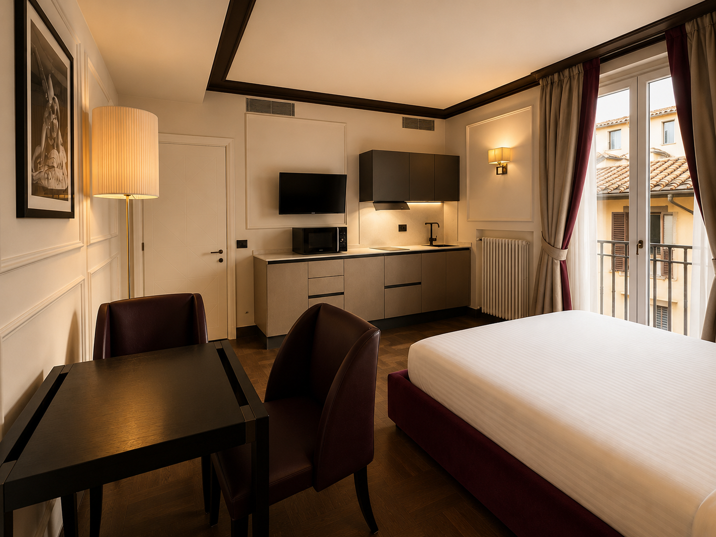 A modern hotel room with a bed, dining table and chairs, kitchenette, and a balcony with a view of neighboring buildings with tiled roofs.