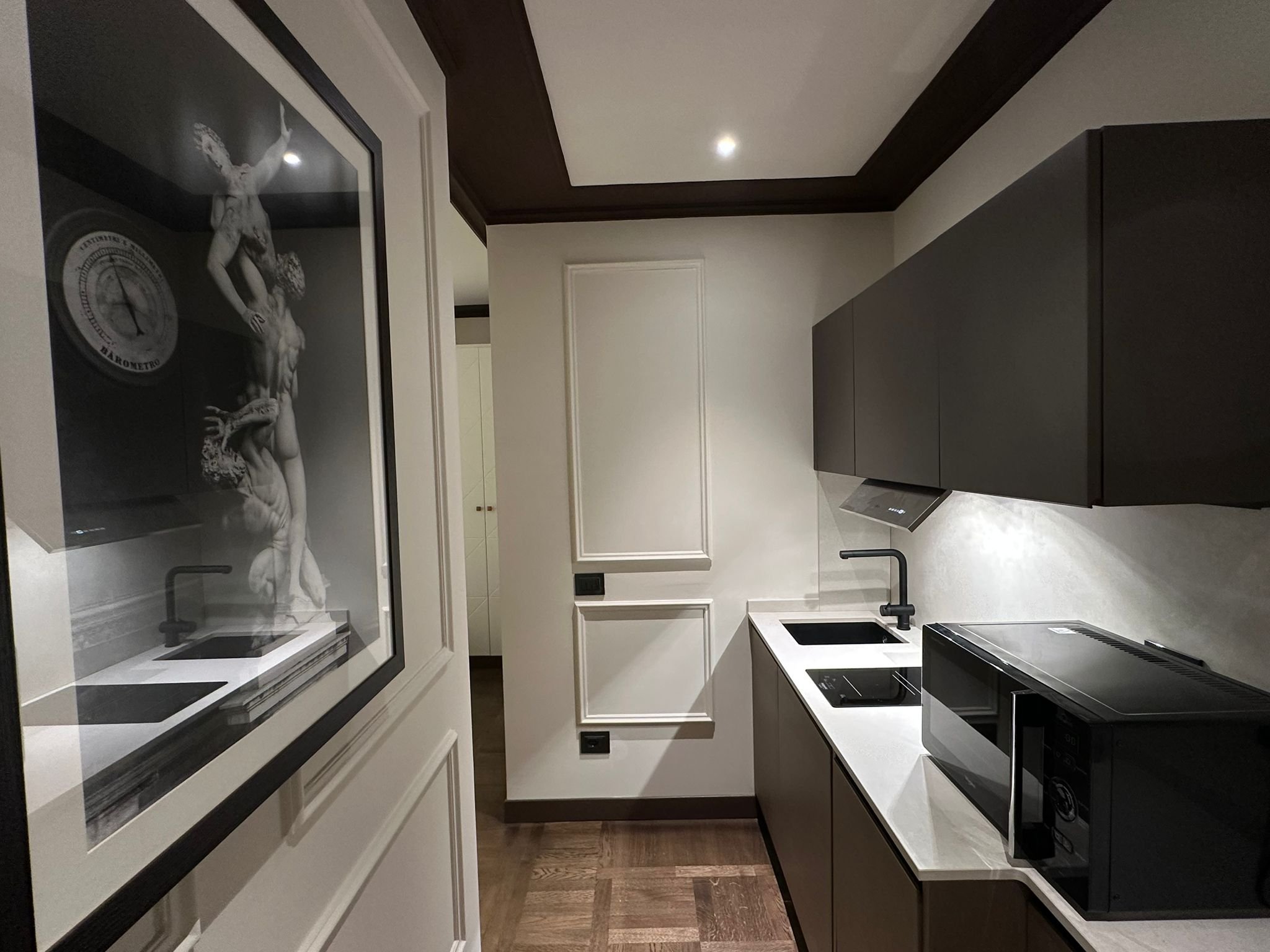 Modern kitchen with black cabinets, white countertops, a black sink, and a black stove. A framed art piece featuring a sculpture and a clock is hanging on the wall.