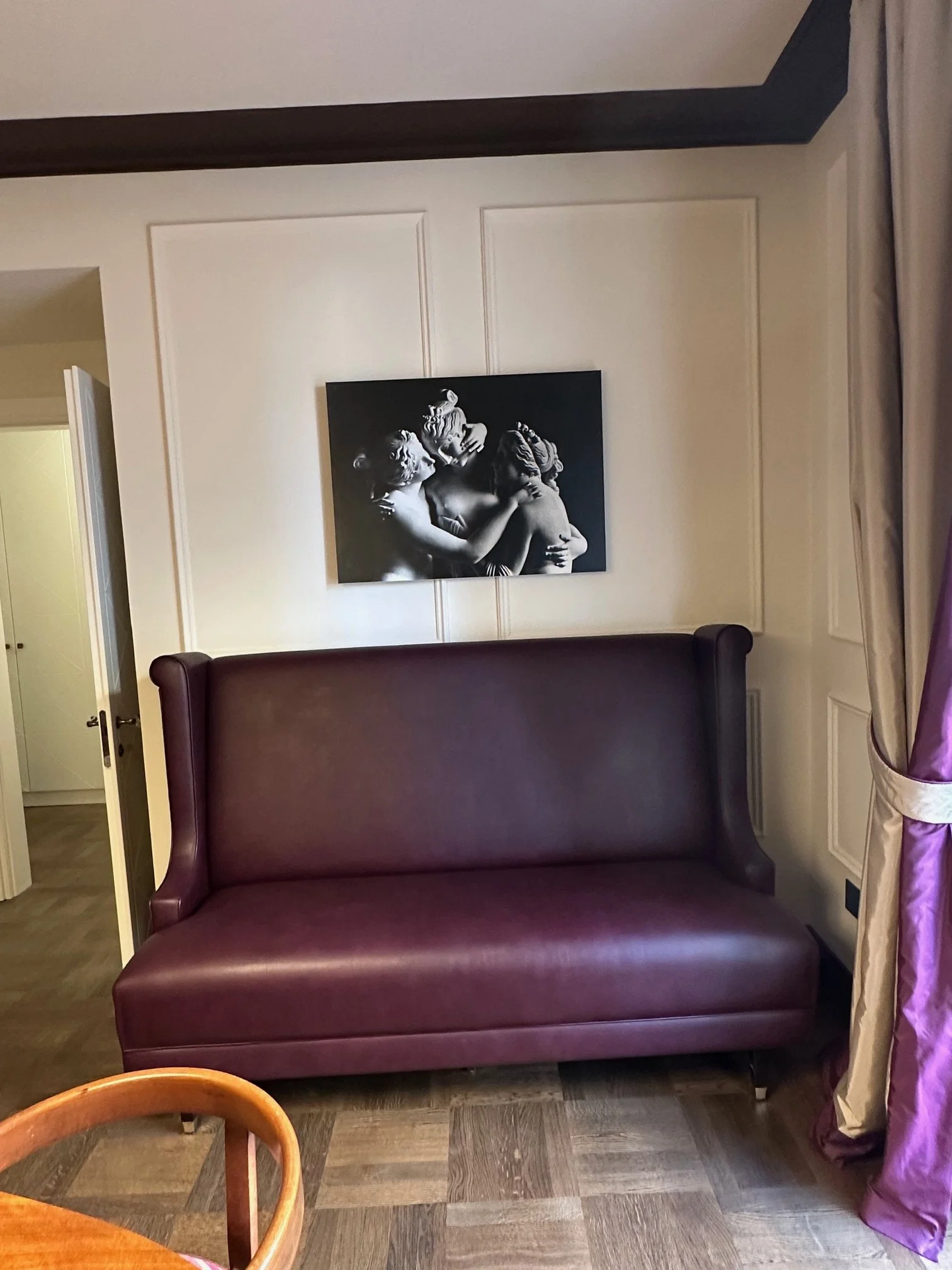 A room with a burgundy leather bed, a floral purple curtain, and a black and white painting of children on the wall