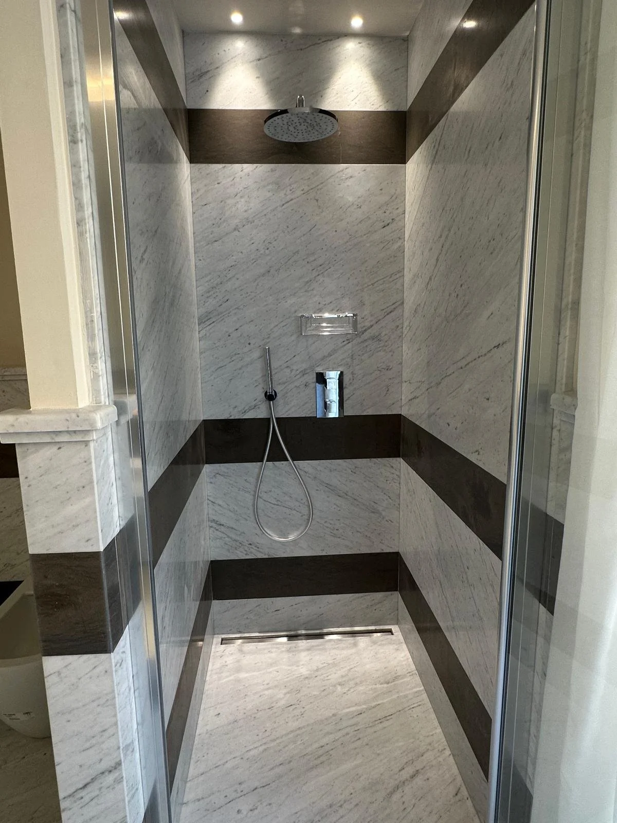 Empty modern shower with white and brown marble tiles, a rain showerhead, and a handheld shower attachment.