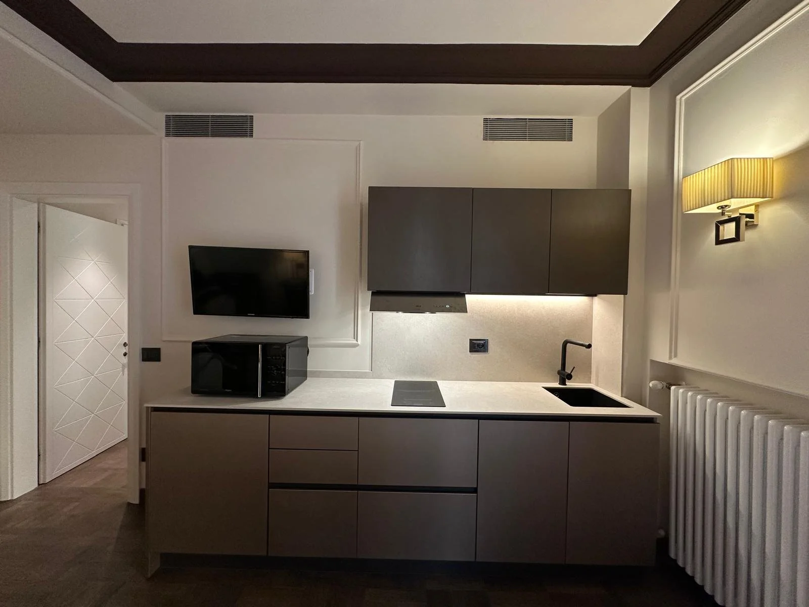 Modern kitchenette with gray cabinets, black faucet, small black microwave, and a wall-mounted TV.