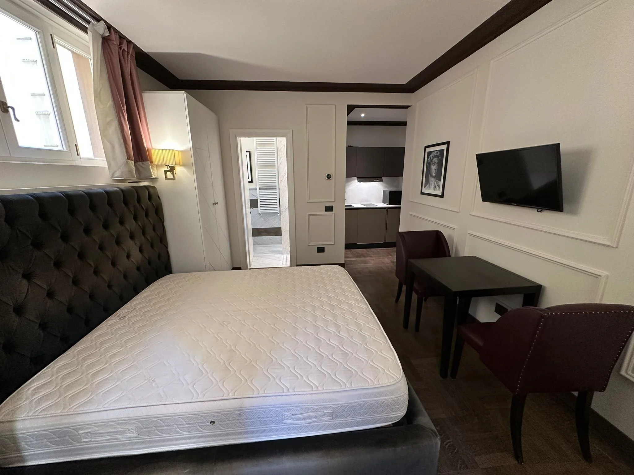 A bedroom with a bed, a picture frame on the wall, a television, and a small table.