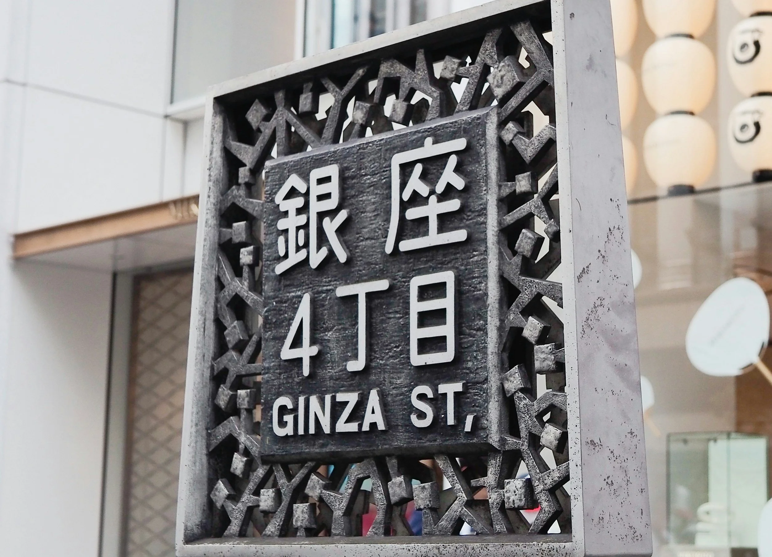 Street sign with Japanese characters and English street names, GINZA STREET, and surrounded by a decorative metal frame.