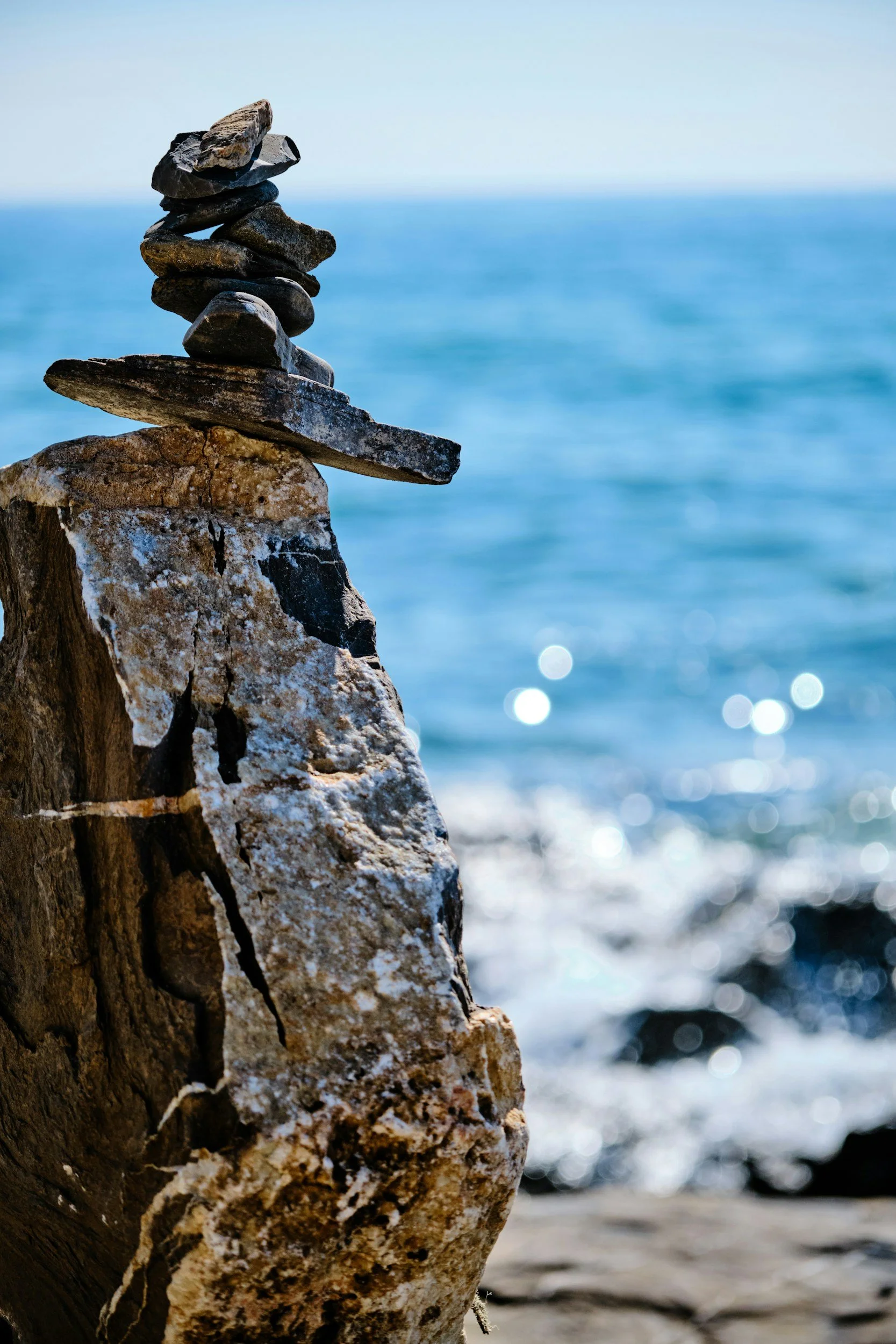 Rock formation with flat rocks stacked on top of each other on a beach with water and horizon in the background.