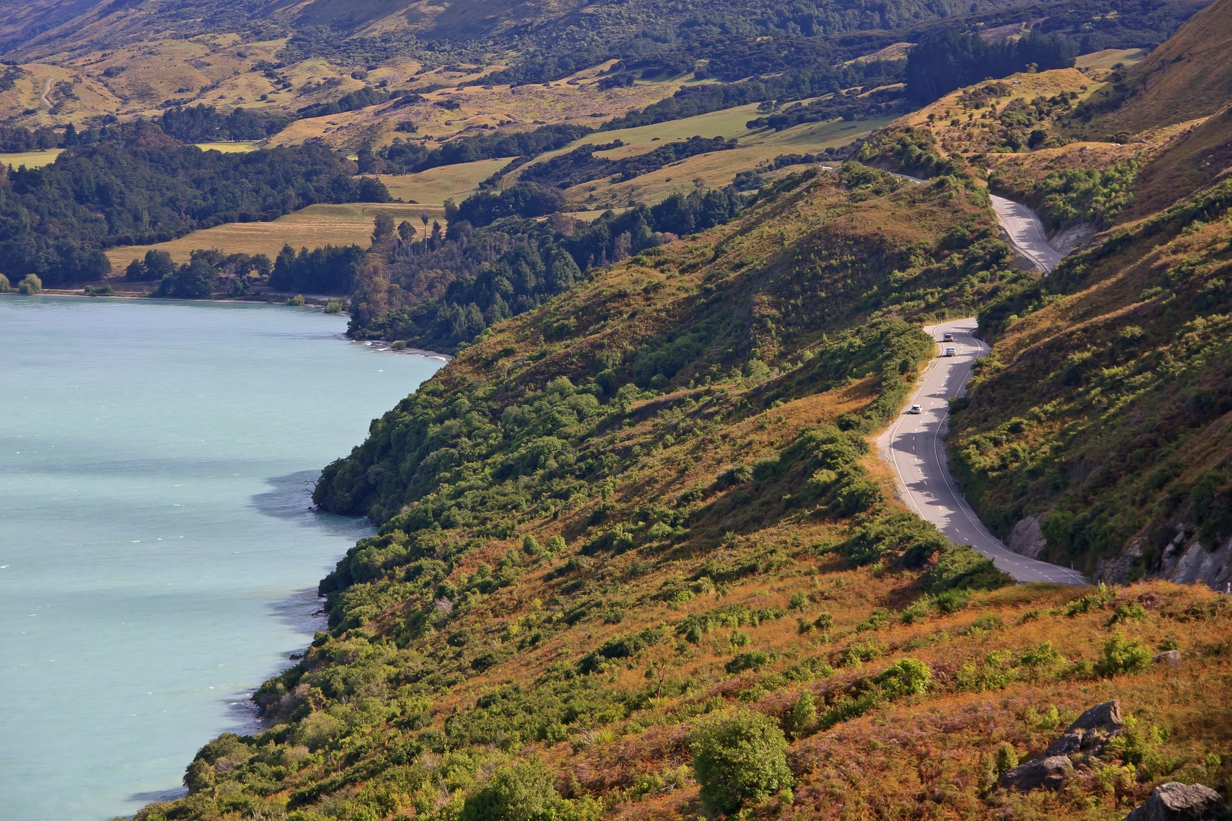 Coastal landscape with a winding mountain road and lush green vegetation.