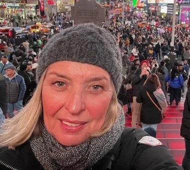 A woman taking a selfie in Times Square, New York City, with a crowd of people and bright billboards in the background.