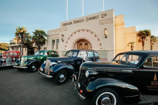 Vintage cars parked in front of the National Tobacco Company building with palm trees nearby.