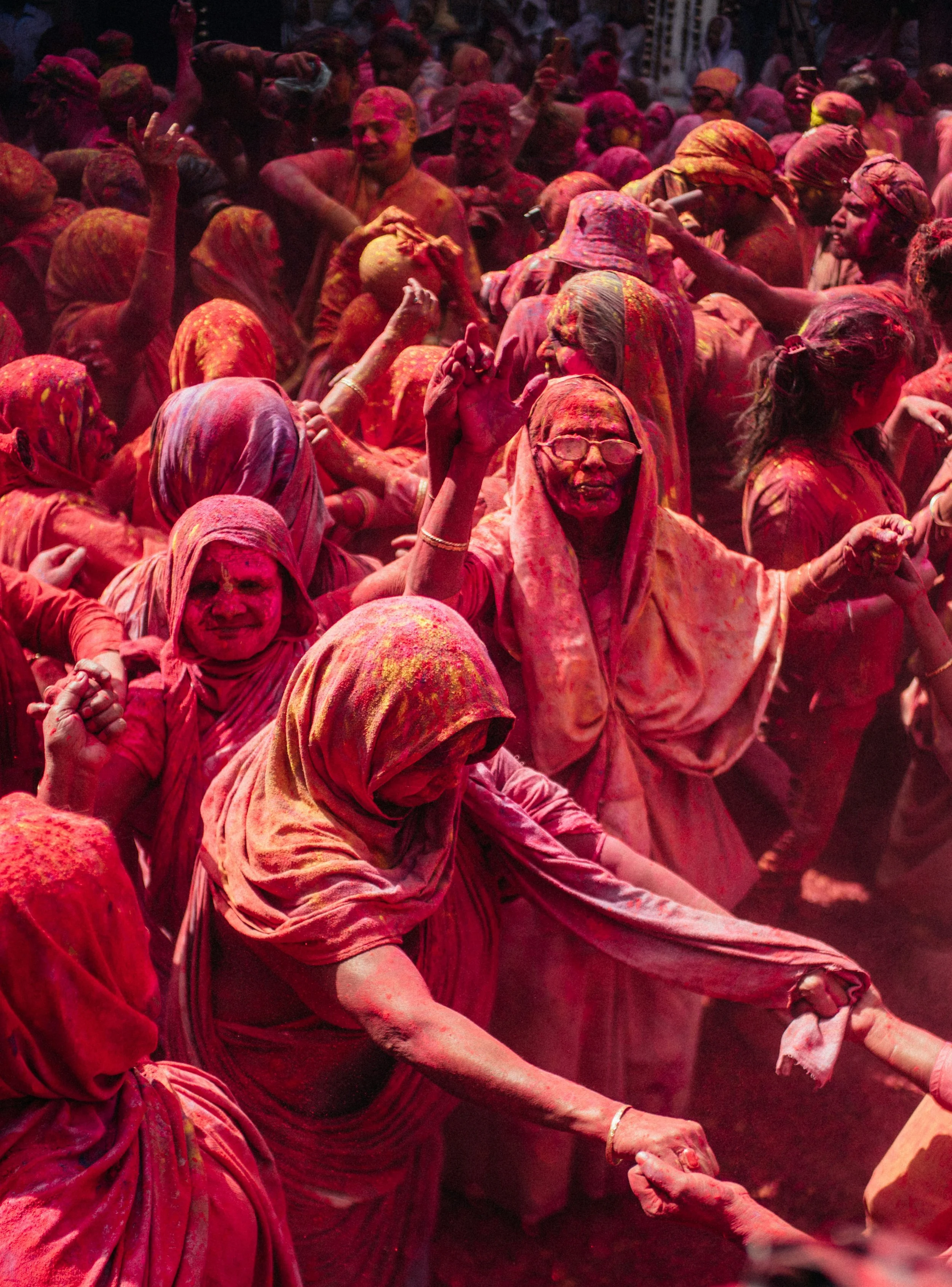 People celebrating Holi by throwing colored powders, with many individuals covered in vibrant colors, engaged in dance and hand-holding.
