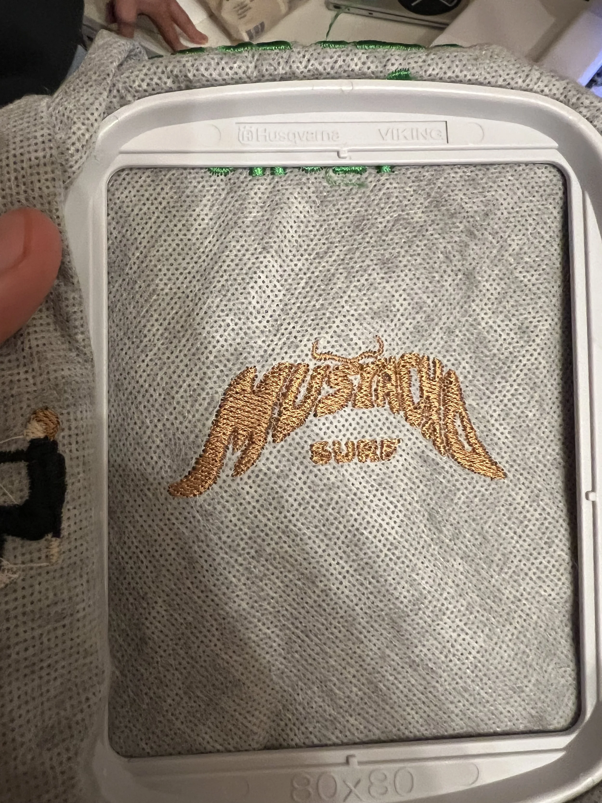 Ein graues Textil mit goldener Stickerei, eingesetzt in einen weißen Rahmen
