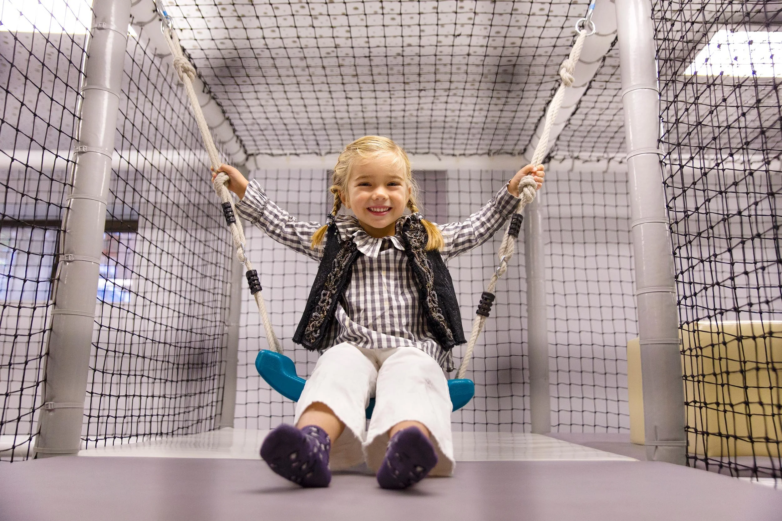 Niña sonriendo en un columpio interior en Columpio Playground, espacio infantil seguro en Chamartín, Madrid.