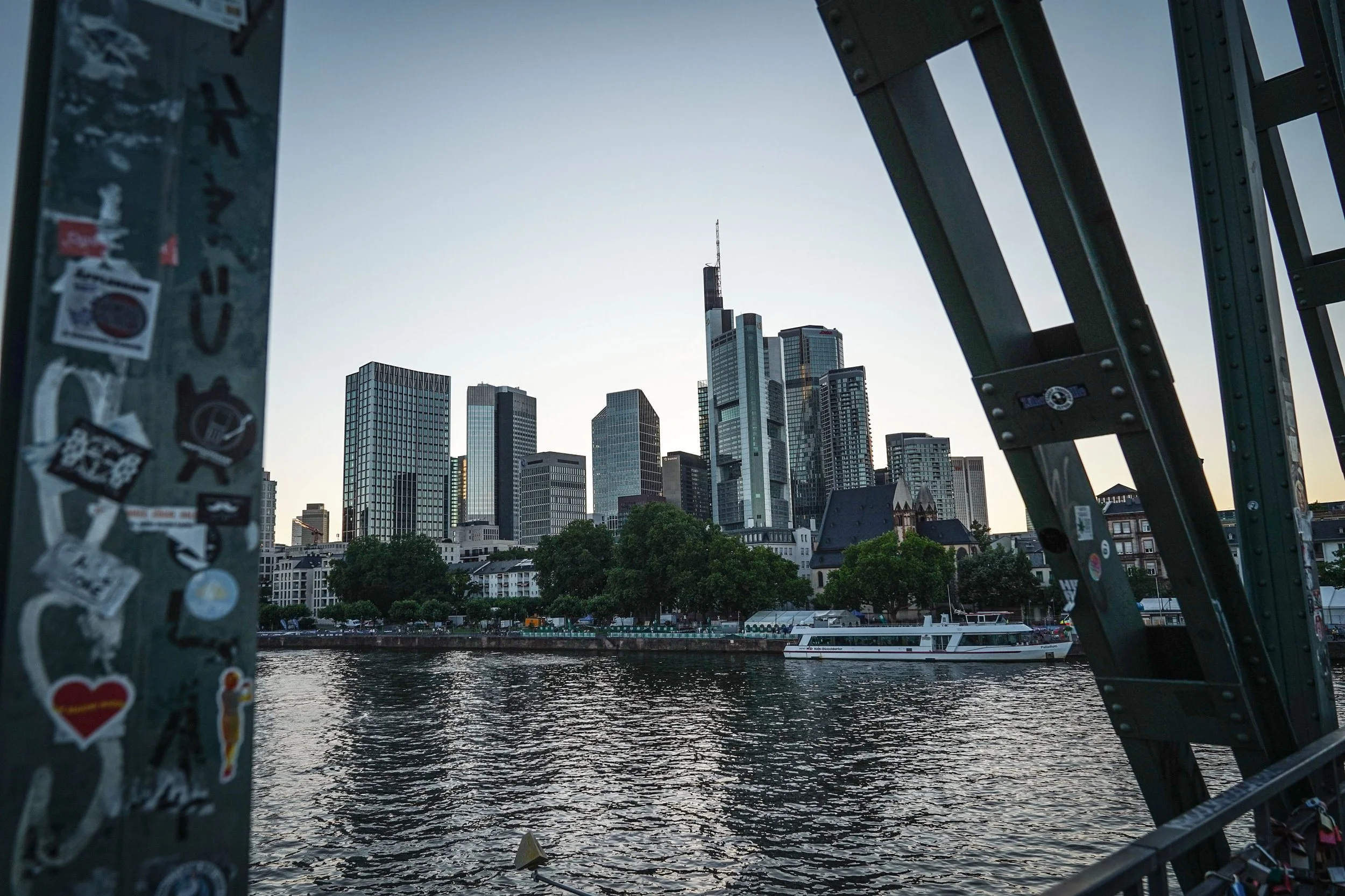 Blick auf eine moderne Skyline mit Hochhäusern, gesehen durch eine Gerüststruktur an einer Brücke mit Aufklebern.