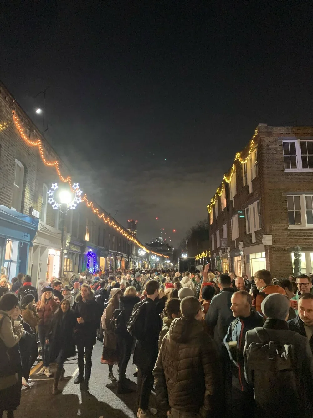 Nighttime street scene with holiday decorations and a large crowd of people in warm clothing.