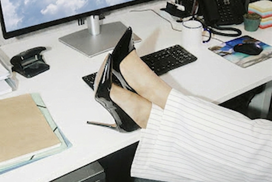 a person in corporate attire resting their legs on top of a computer desk