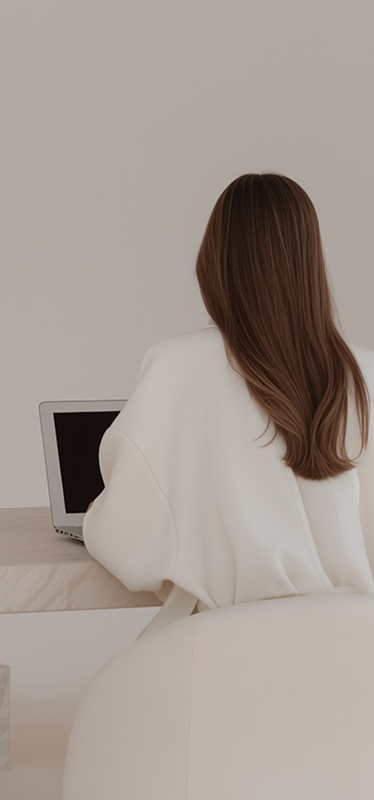 Aoife sitting at a minimalist desk using a laptop, viewed from behind in a calm, neutral-toned workspace.