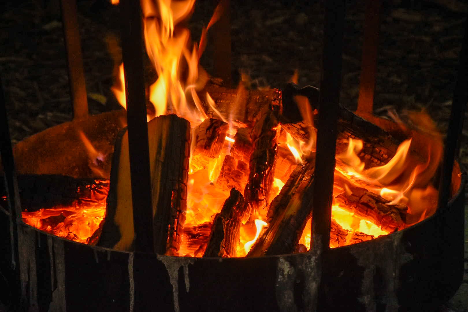 A close-up of a fire burning inside a metal fire pit or brazier, with visible wood logs and flames.