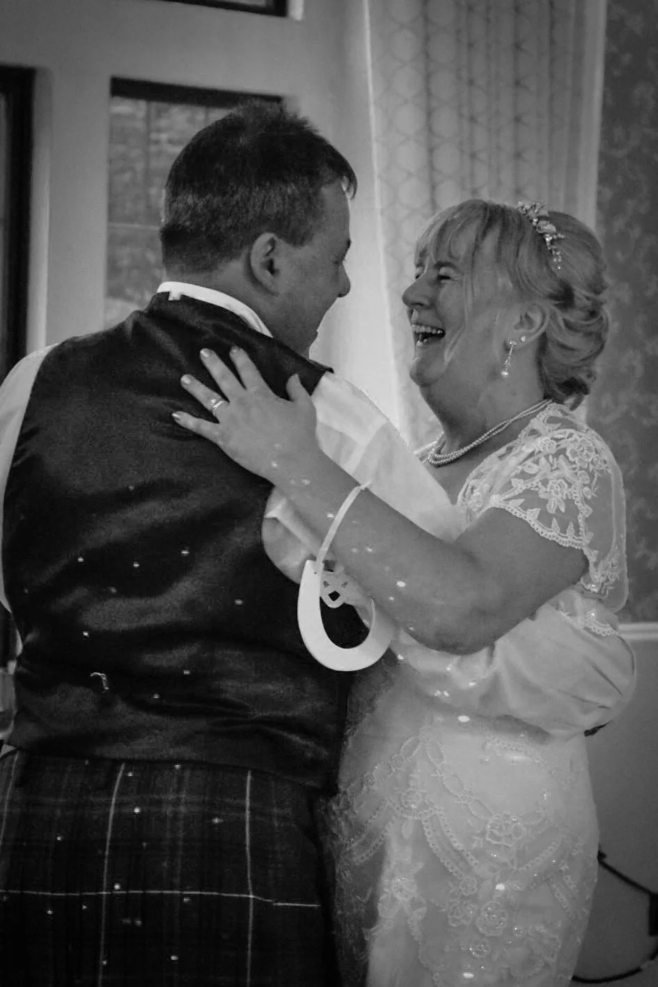 A joyful bride and groom share a dance, smiling and looking at each other, during their wedding reception in a decorated indoor venue.