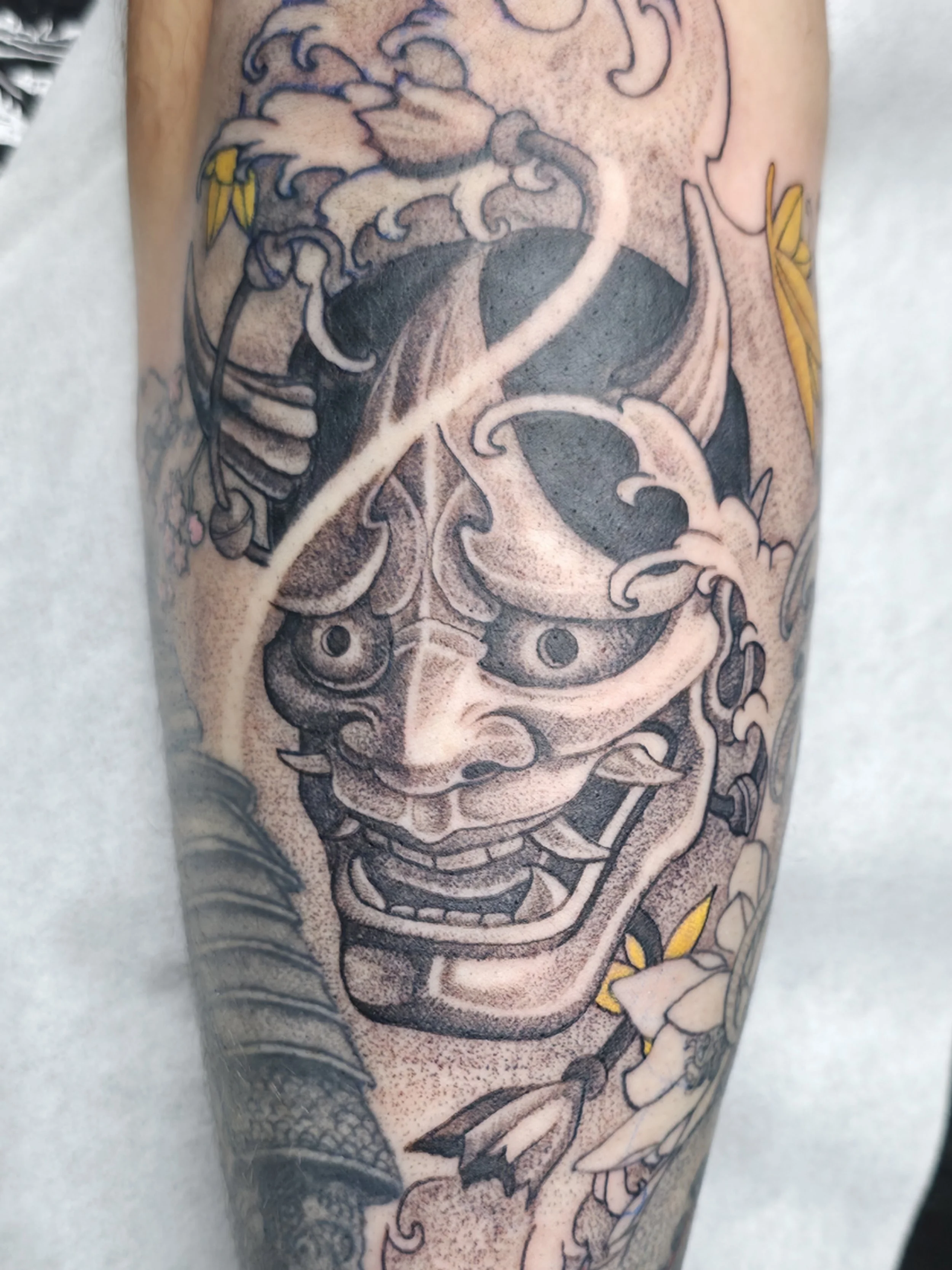 Close-up of a tattoo on a person's arm depicting a stylized dragon with intricate shading, line work, and some yellow accents.