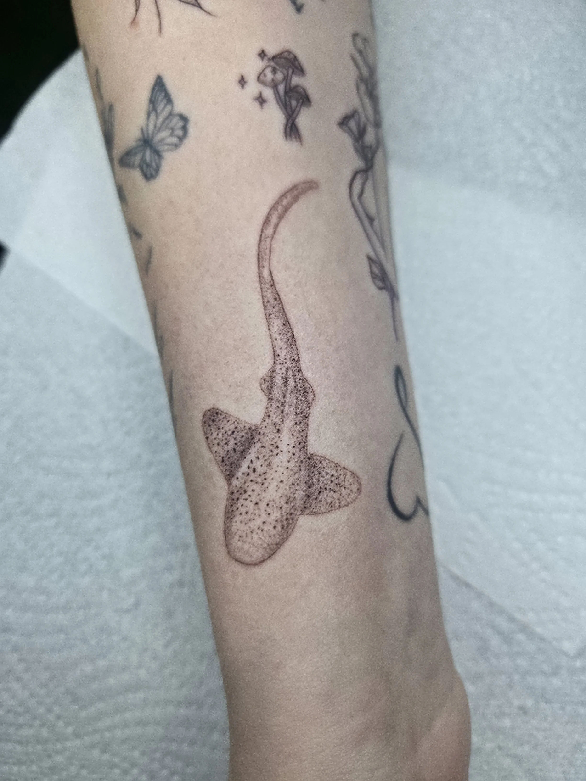A tattoo of a face outline with a dotted texture on a person's skin, with butterflies and small decorative elements around it.