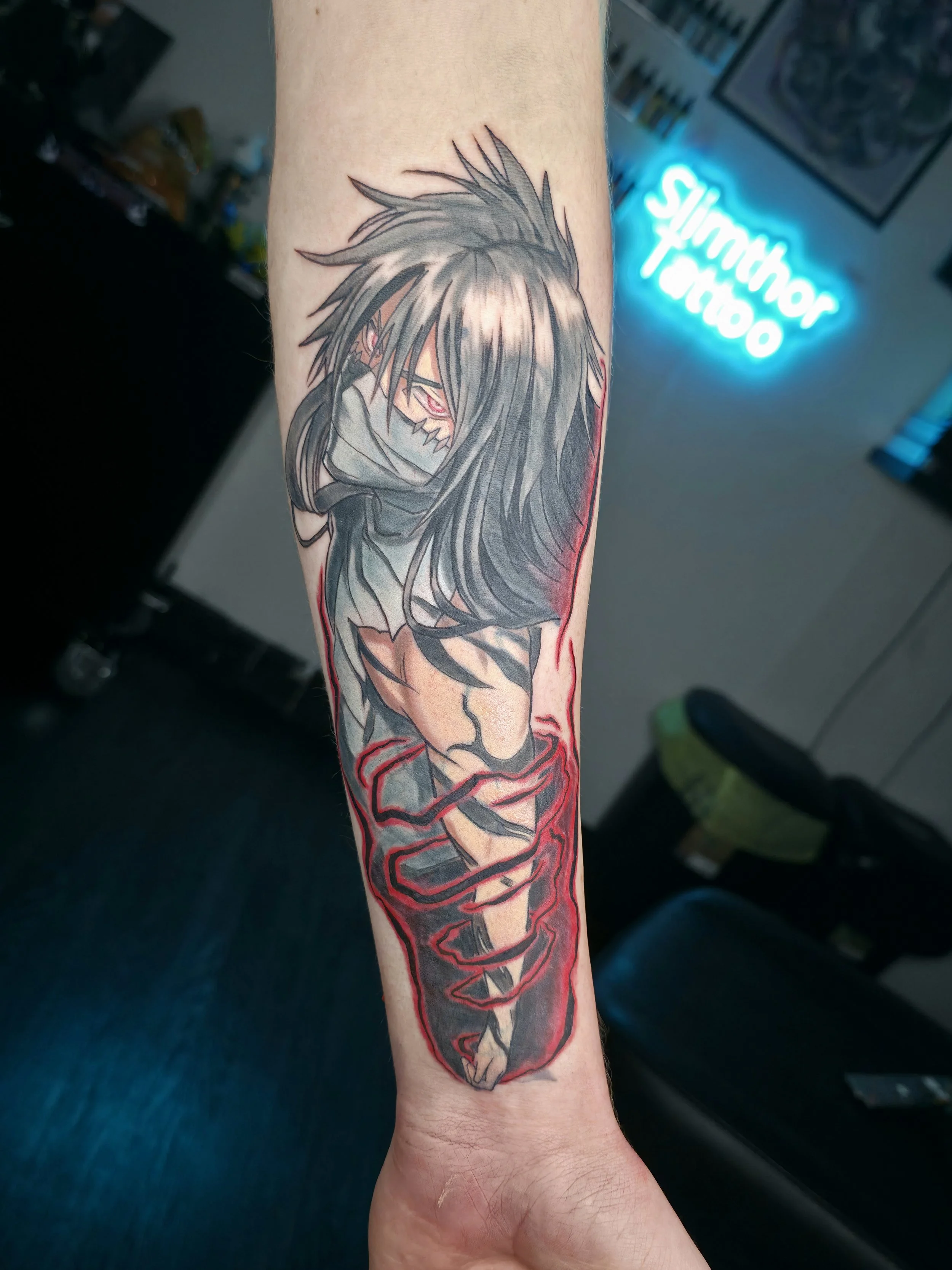 Tattoo of a stylized anime character with spiky hair, red eyes, and wearing a hoodie, located on a person's forearm.