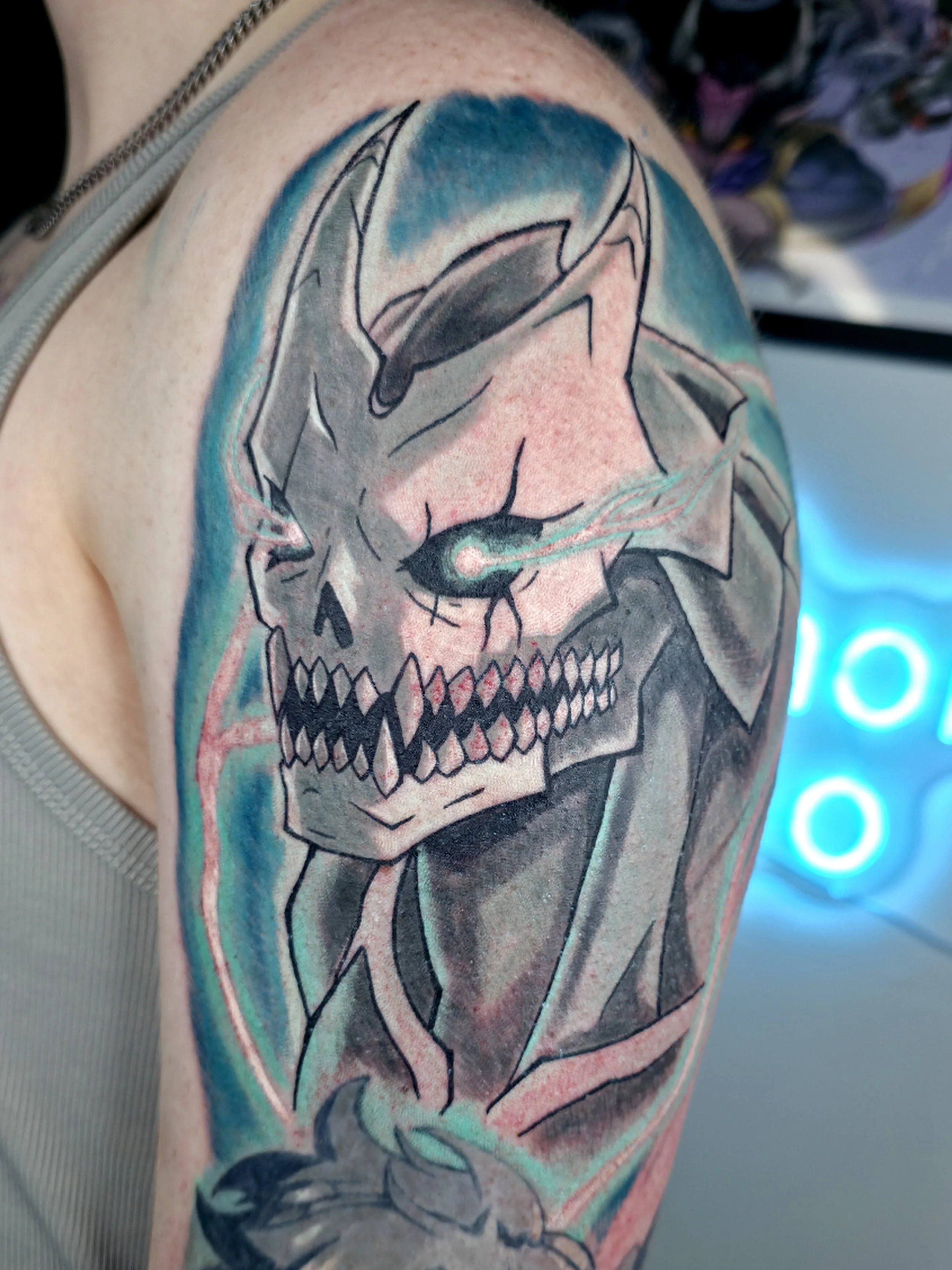 Colorful tattoo of a skull with a rabbit nose, large eye, and a hat on the upper arm, with vibrant blues, pinks, and blacks.