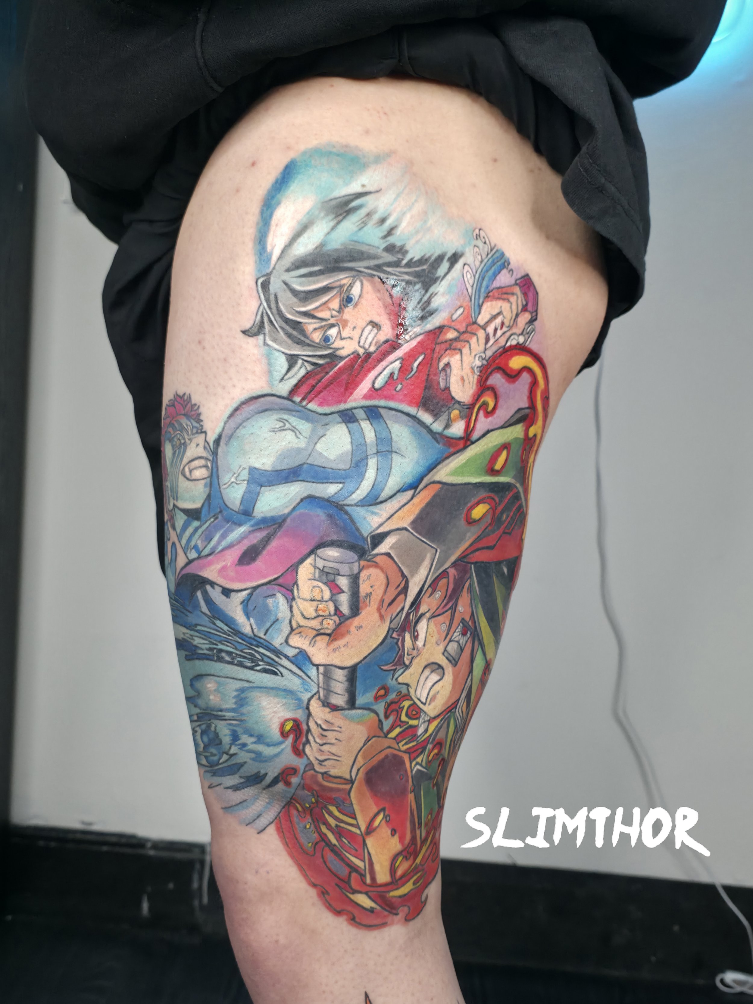 Colorful tattoo on a person's thigh depicting a fierce anime-style character with silver hair, wielding a sword, and flames surrounding the character. The tattoo features vibrant colors including red, blue, and orange, with detailed shading and line work.
