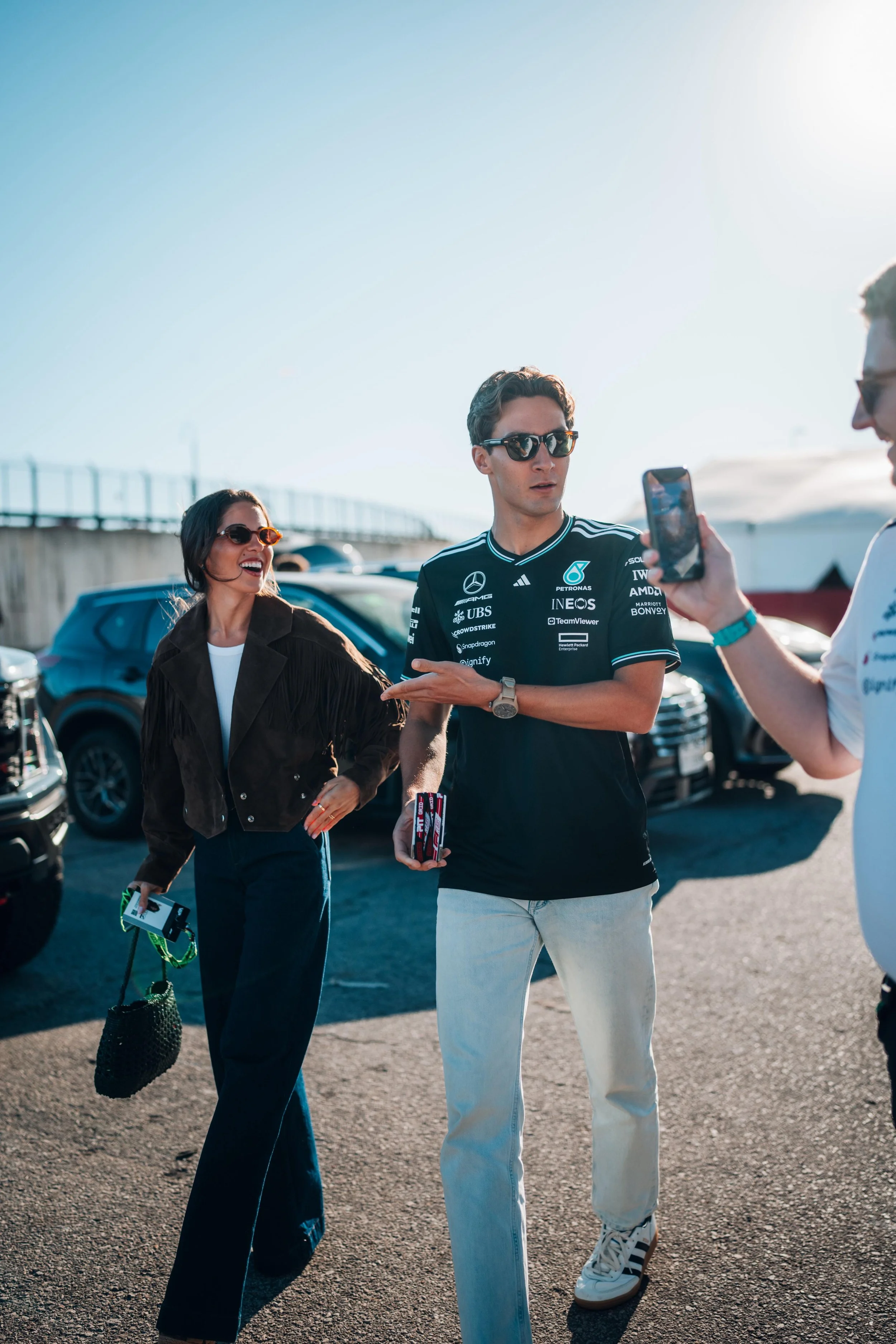George Russell and his girlfriend Carmen walk through a car park with Jack Leslie filming them on his phone.