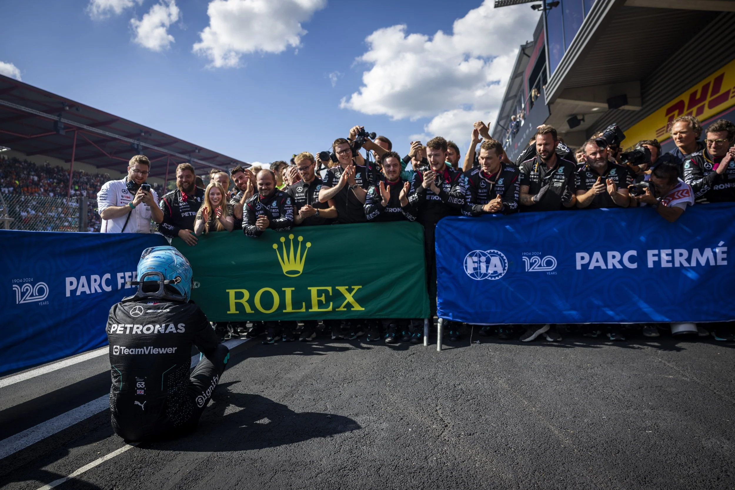Formula 1 team members celebrating in the pit lane, with a driver kneeling in front, at a racing event.