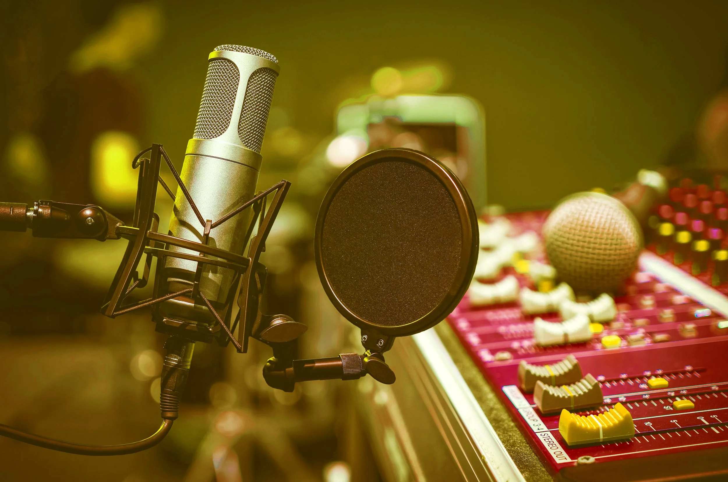 A recording microphone with a pop filter in a sound studio, with audio mixing equipment in the background.