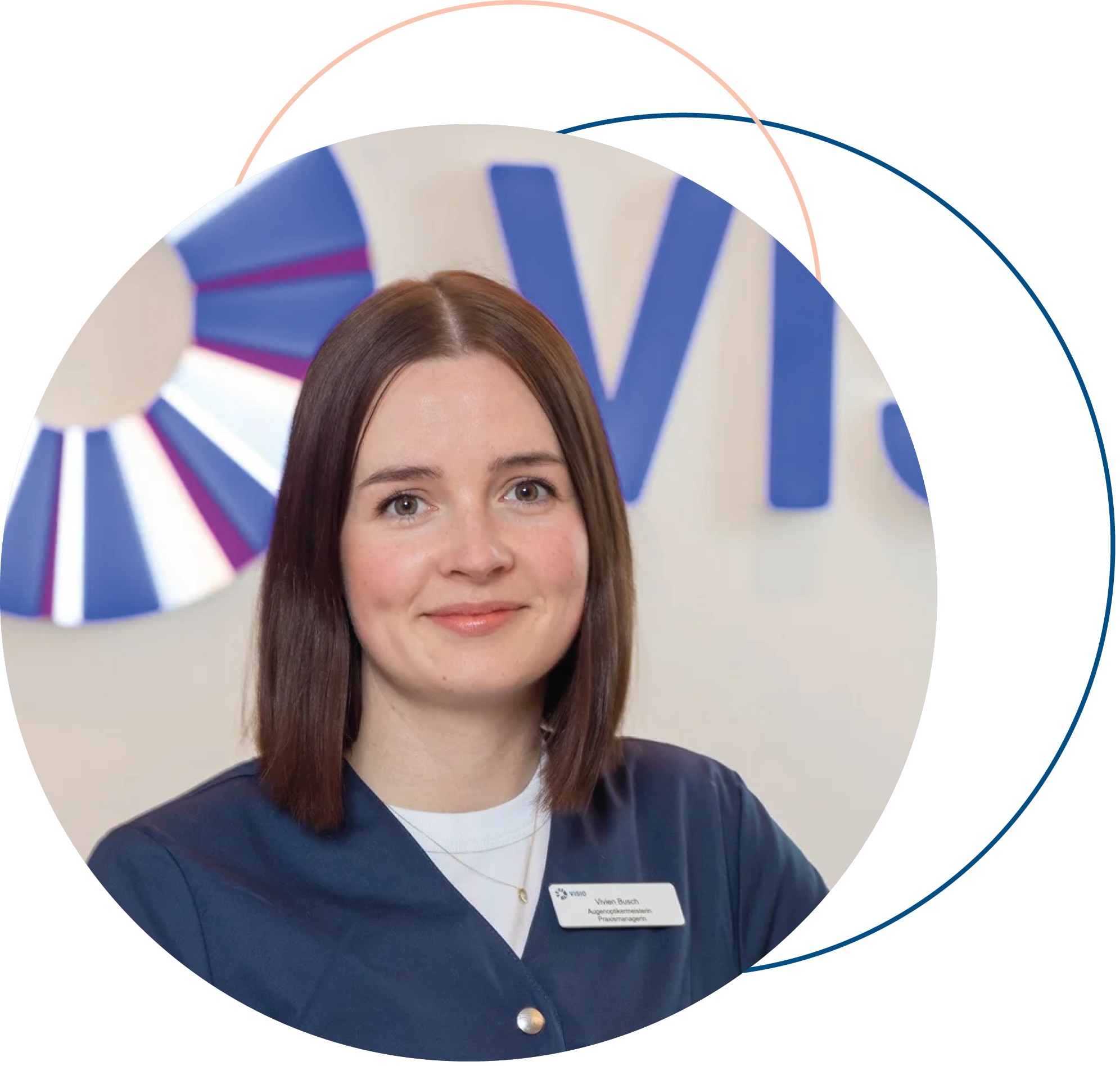 Nahaufnahme einer Frau mit braunen, schulterlangen Haaren, die einen blauen Blazer und eine weiße Bluse trägt, vor einem blauen und weißen Hintergrund mit einem großen Logo. Sie trägt eine Namensschild mit ihrem Namen "Vreno Bausch" und ihrer Position. Sie lächelt leicht und schaut direkt in die Kamera.