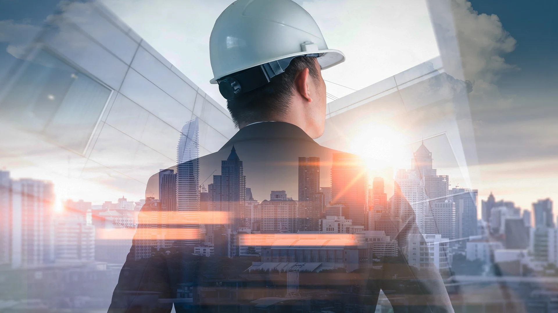 A double exposure image of a man wearing a white hard hat looking at a city skyline during sunset, with glass reflections and building overlays.
