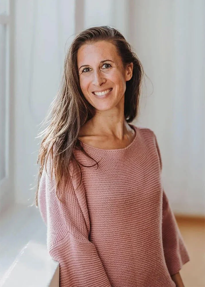 Ein Porträtbild von Maria Lötcher. Sie lächelt in die Kamera, trägt langes, offenes, hellbraunes Haar und einen rosa Pullover.