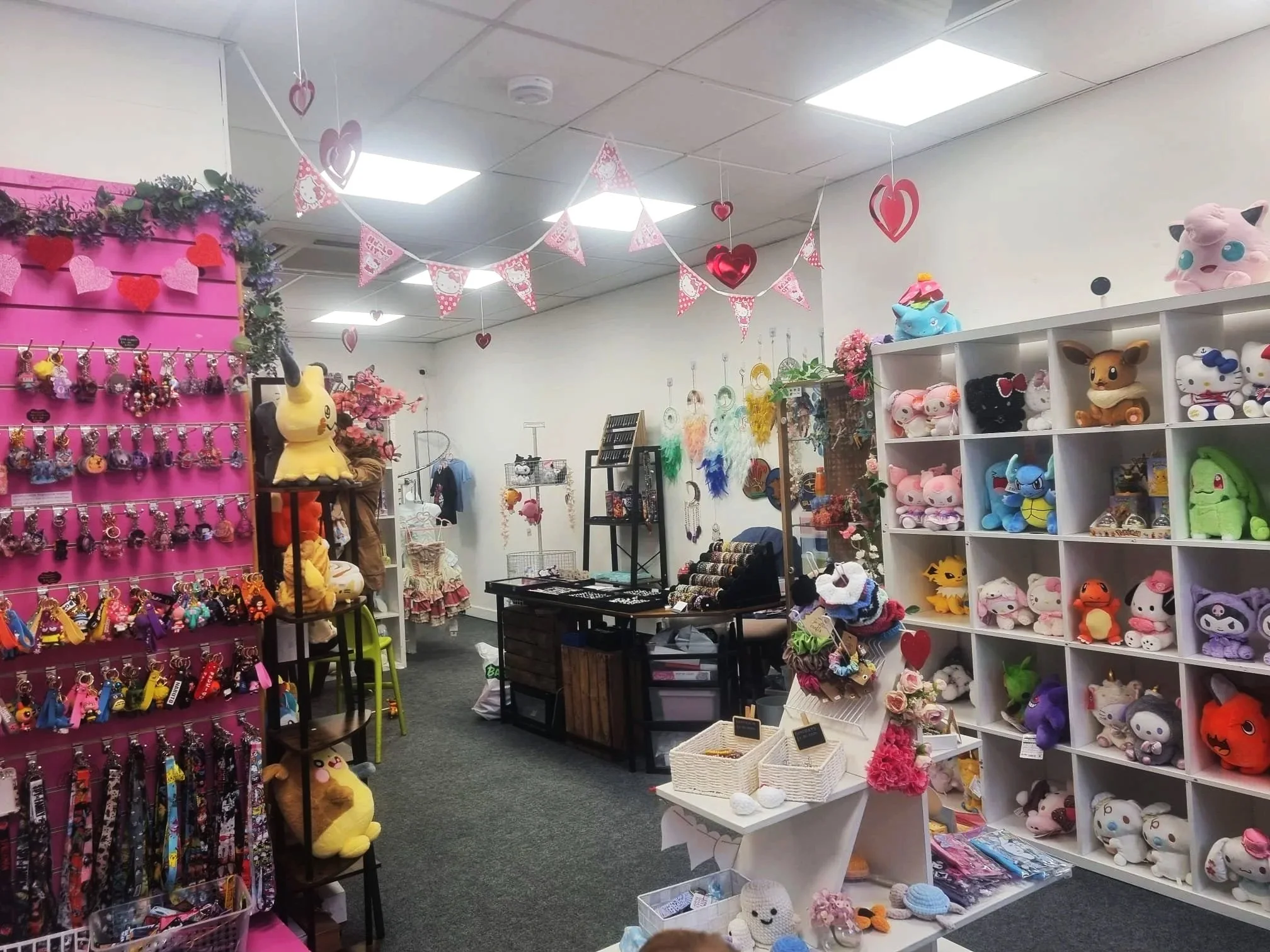 A store filled with plush toys, keychains, and accessories, decorated with pink and red heart and Valentine-themed decorations hanging from the ceiling.