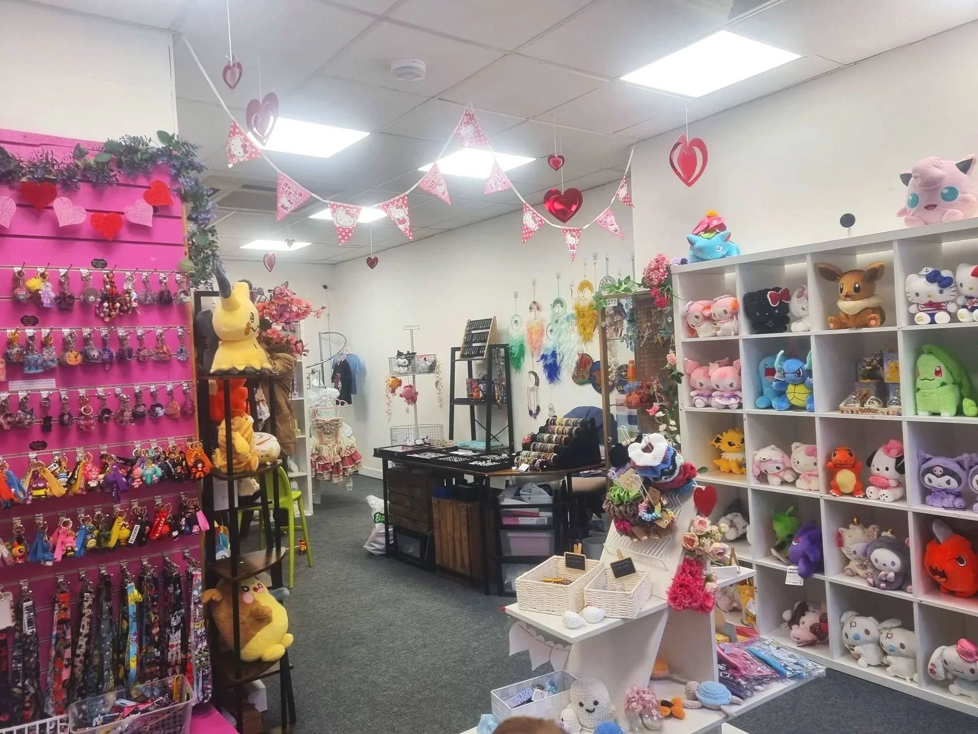 A toy store decorated with pink and red heart-shaped decorations for Valentine's Day, featuring plush toys, keychains, and other merchandise.