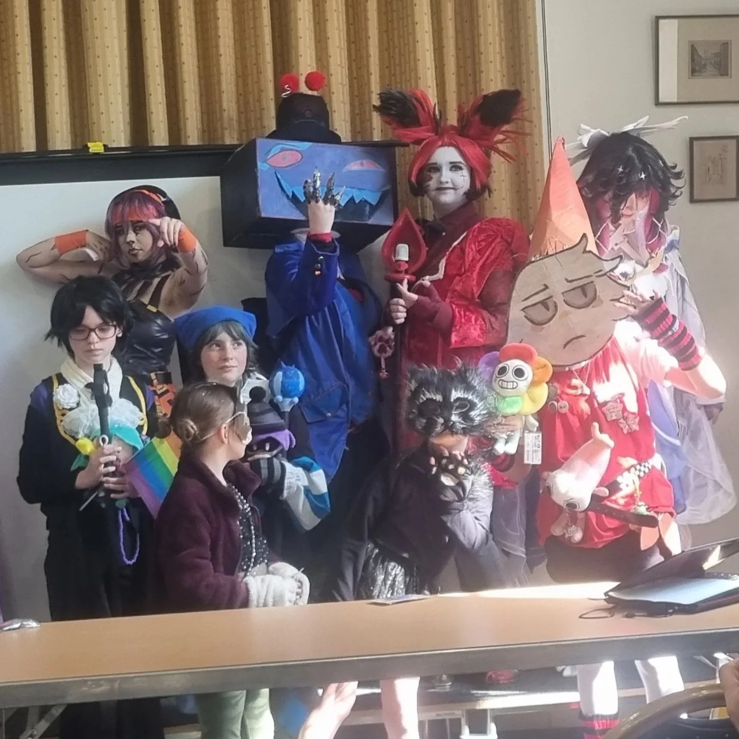 Group of children and adults in colorful costumes, some with masks, at a party or cosplay event.