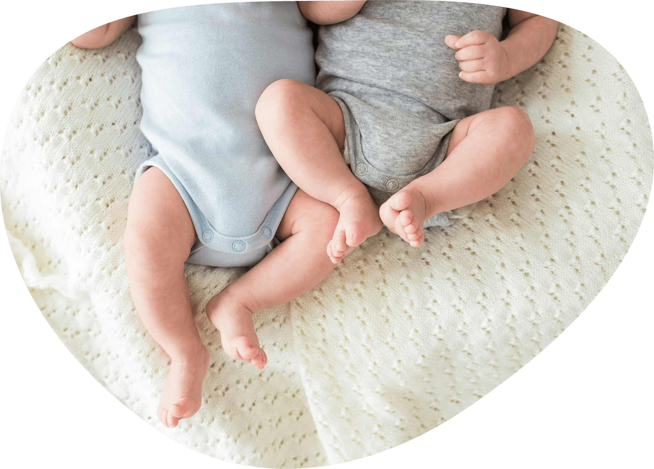 Zwei Babys ruhen nebeneinander auf einem cremefarbenen, gestrickten Tuch.